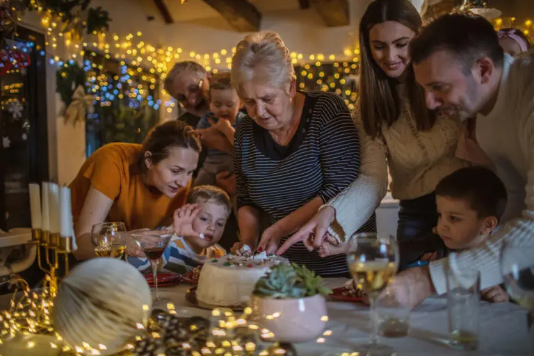 In-laws and family sharing holiday traditions at dinner table, as grandmother serves dessert under twinkling Christmas lights